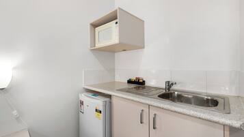 Eine kompakte Küche mit integriertem Mikrowellenherd, einer Edelstahl-Spüle und einem kleinen Kühlschrank.