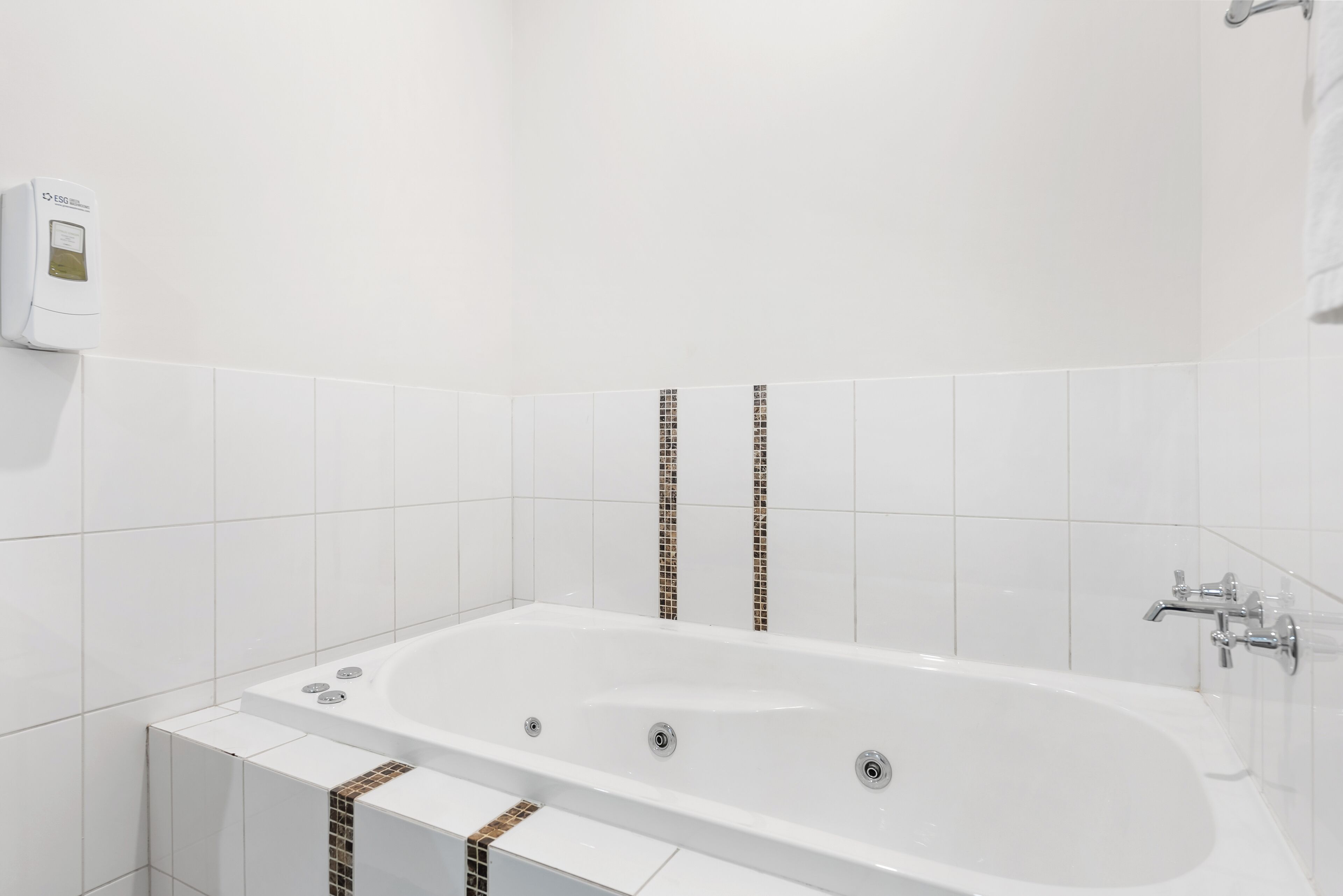 A modern bathroom with a freestanding bathtub, white tiles, and a visible water heater on the wall.