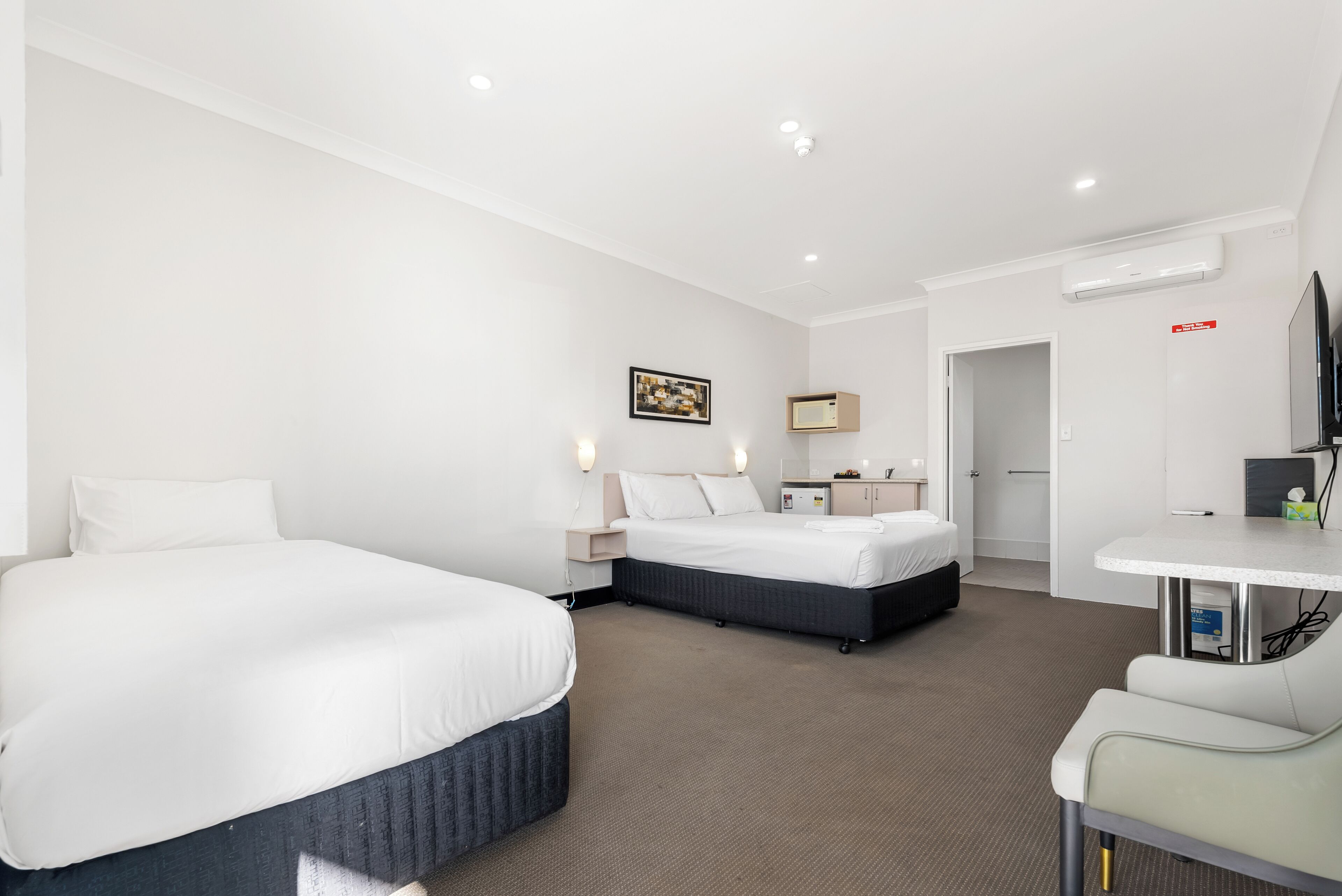 Habitación de hotel con dos camas, un escritorio, una silla, un televisor, un microondas y una puerta que da a otra habitación.