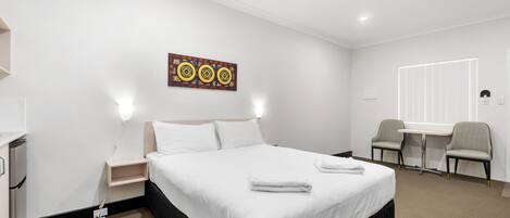 Ein Hotelzimmer mit einem Bett, Nachttischen, einem Schreibtisch mit zwei Stühlen und einem an der Wand hängenden Kunstwerk.