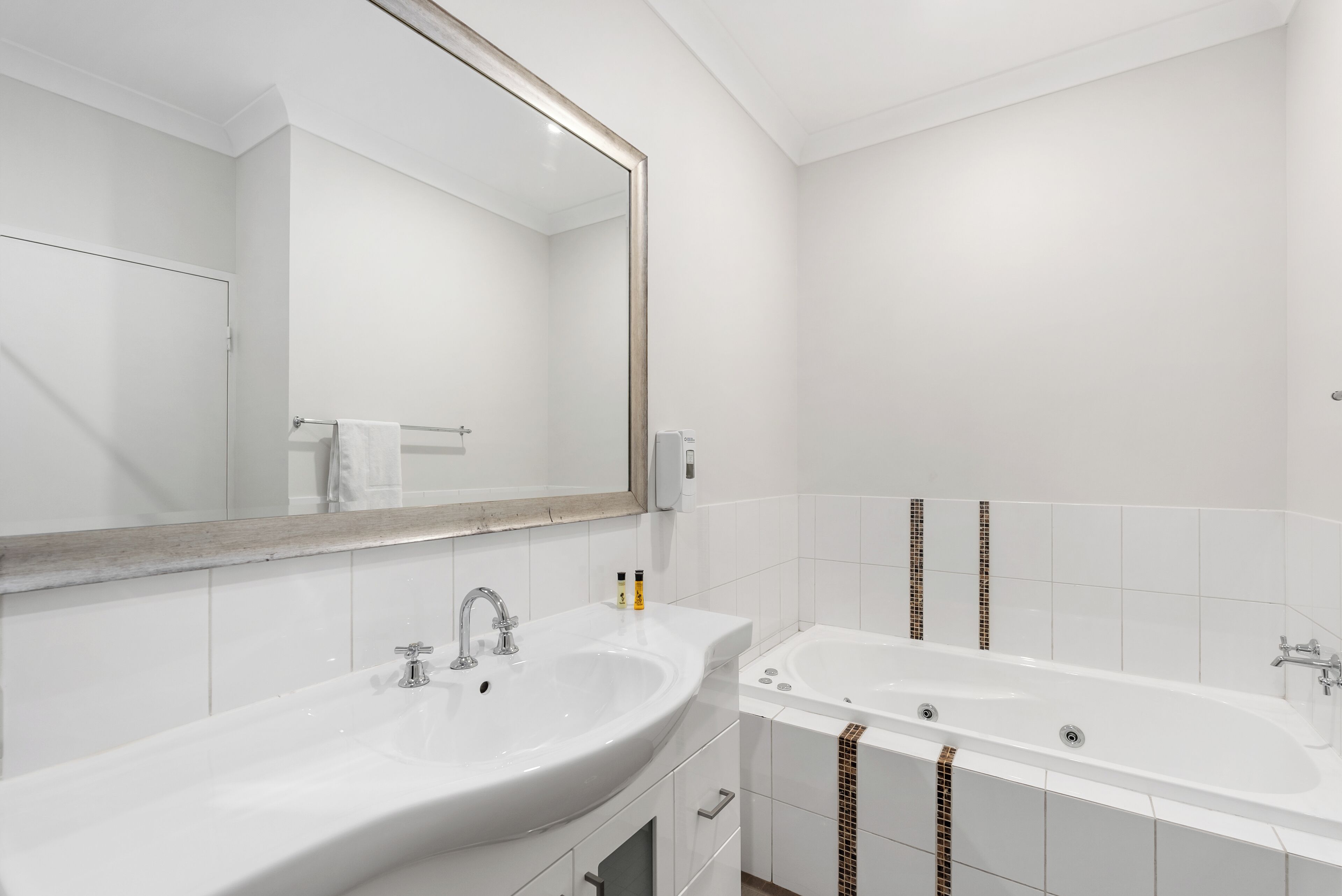 Un baño moderno con un espejo grande, un lavamanos y una bañera.