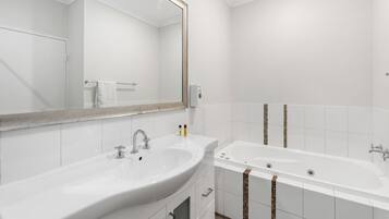Un baño moderno con un espejo grande, un lavamanos y una bañera.