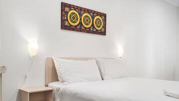 A neatly made bed with white linens, a wooden headboard, and two bedside lamps.