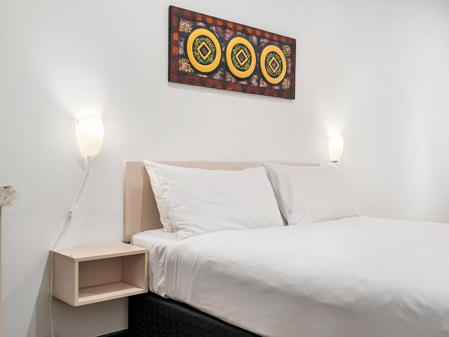 A neatly made bed with white linens, a wooden headboard, and two bedside lamps.
