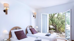 A modern hotel room with two beds, each with a wooden headboard, white bedding, and a view of a rocky landscape through a glass door. - Stylish Contemporary Villa with Heated Pool near Beach and Restaurant (Corbara)
