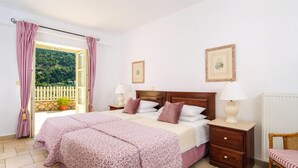 A bedroom with a bed, two bedside tables with lamps, a chair, and a view of greenery through a window. - Cosy Villa with Sea-and-Mountain Views near Agios Nikitas (Lefkada)