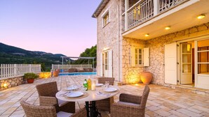 A stone house with a pool, outdoor dining area, and a view of the hills. - Cosy Villa with Sea-and-Mountain Views near Agios Nikitas (Lefkada)
