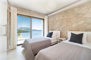 Ein Hotelzimmer mit zwei Betten, einer Steinsäule und einem großen Fenster mit Blick auf das Meer und die Berge.