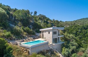 Eine moderne Villa mit Swimmingpool, Steinmauern und Blick auf die umliegenden bewaldeten Hügel.