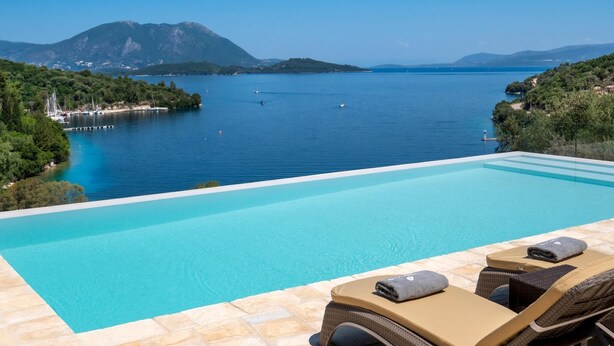 Una piscina infinita con vistas despejadas al mar tranquilo y montañas lejanas.