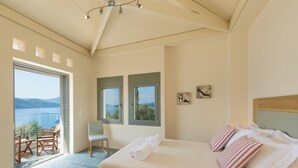 Ein Schlafzimmer mit einem großen Bett, zwei Fenstern, einem Sessel und Meerblick.