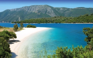 Una playa con aguas turquesas cristalinas, arena blanca y colinas verdes al fondo.