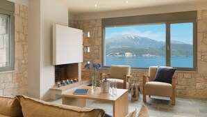 Ein modernes Wohnzimmer mit Steinwänden, einem Kamin, einer Couch und Blick auf eine gebirgige Küstenlandschaft.