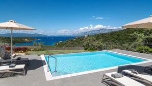 A swimming pool with lounge chairs and umbrellas, overlooking a coastal landscape with mountains and the sea. - Stylish Contemporary Villa with Sea Views near Vathy Tavernas (Meganissi)