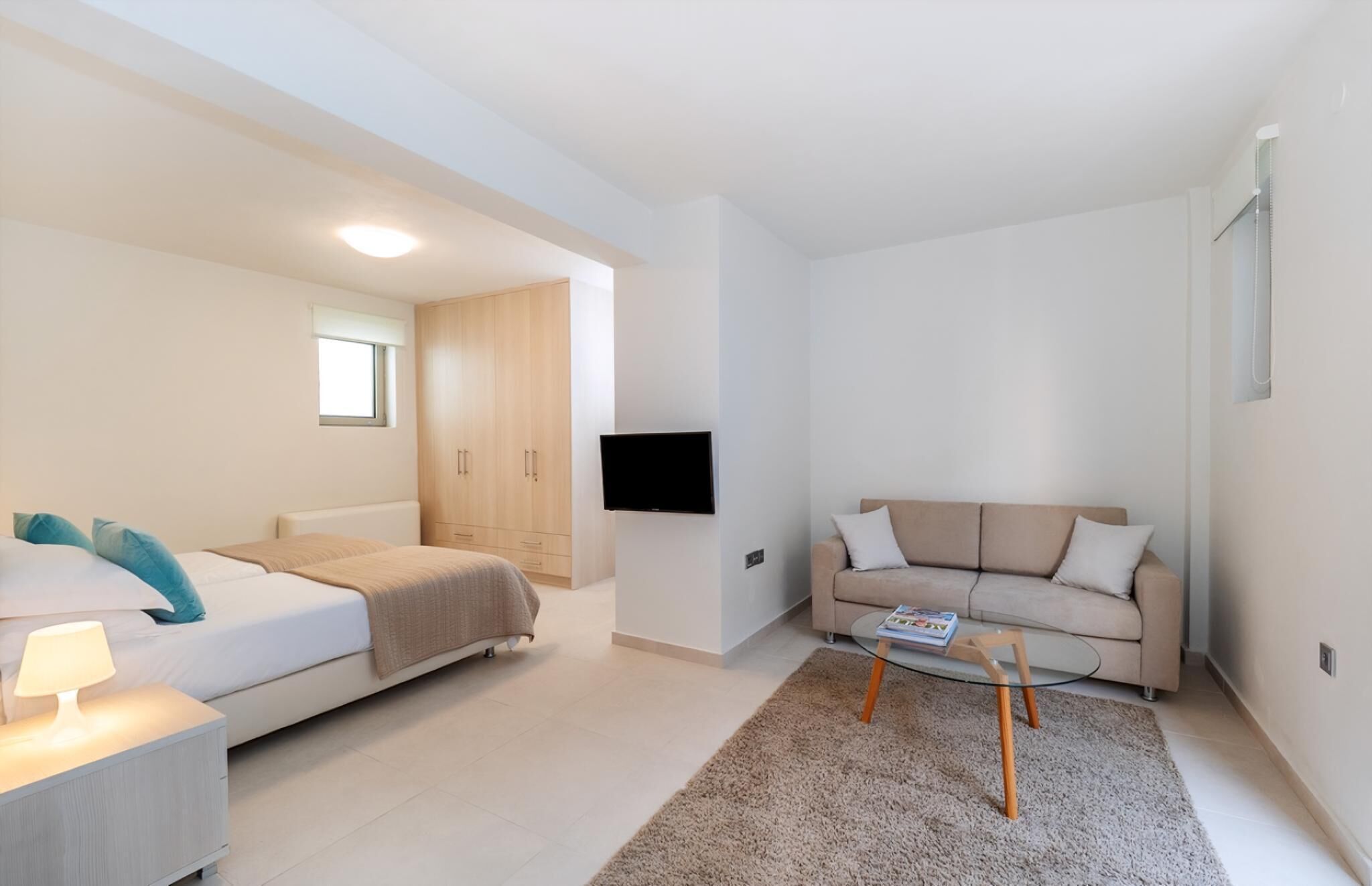 Ein modernes, gut beleuchtetes Schlafzimmer mit Bett, Nachttisch und einem an der Wand montierten Fernseher.