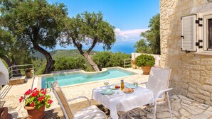 A stone building with a pool, outdoor seating, and a view of the sea. - Cosy Round House for Adults with Stunning Sea & Island Views (Paxos)