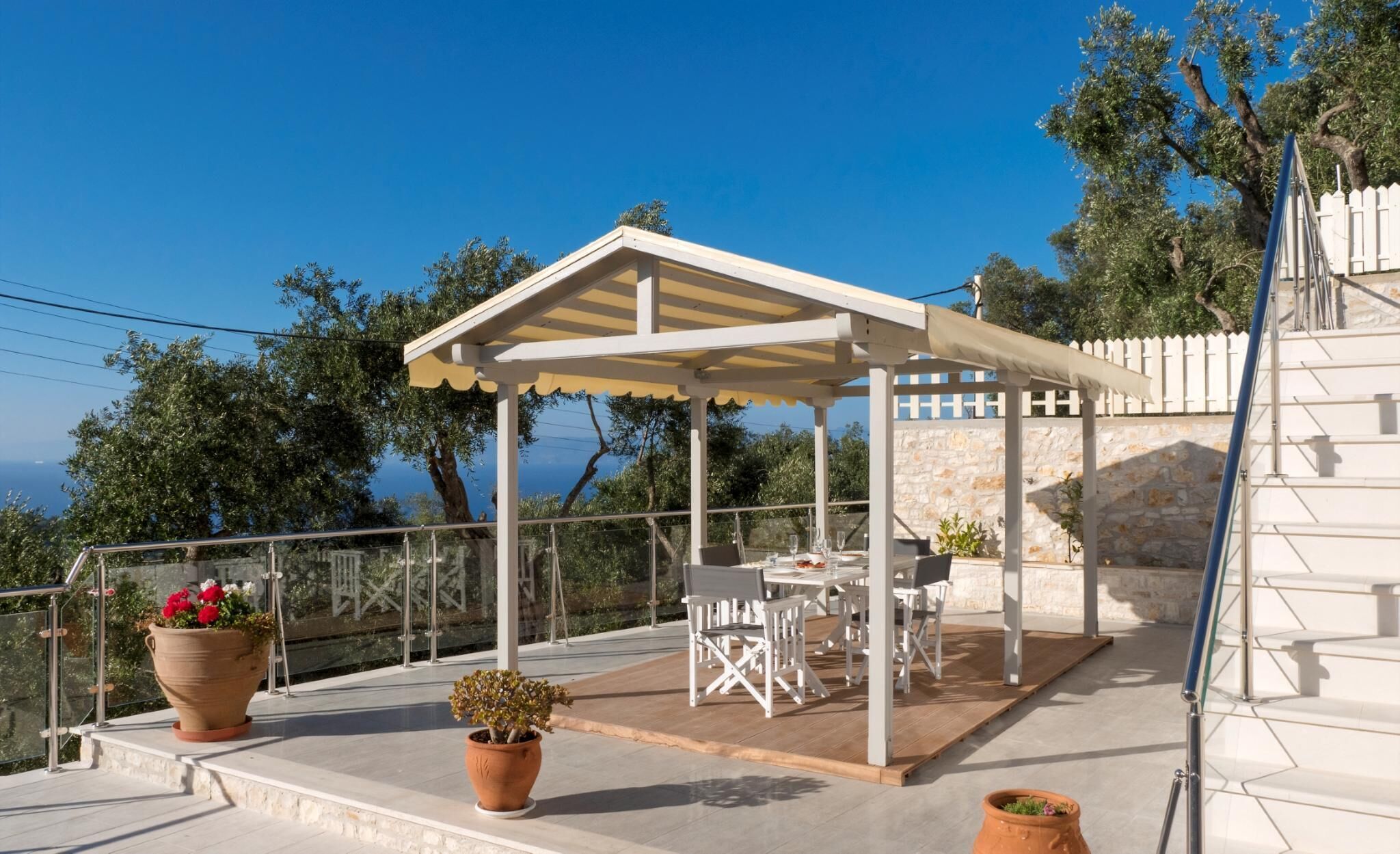 An outdoor patio with a covered seating area, a table, and chairs. There are potted plants on the terrace.