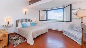 Ein Schlafzimmer mit einem Bett, zwei Nachttischlampen, einem Fenster mit Blick, einem Heizkörper und einem Sofa.
