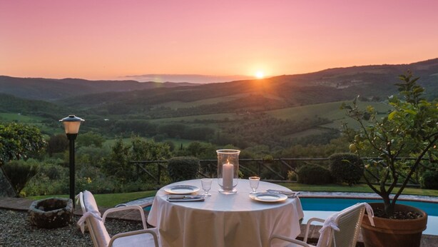 Ein runder Esstisch mit Kerzenarragement, mit Blick auf eine malerische Landschaft mit Hügeln und einem Pool.