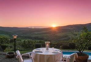 A round table set for dining with a candle centerpiece, overlooking a scenic landscape with hills and a pool. - Private Pool Retreat in Chianti (Radda in Chianti)