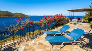 Une terrasse avec un sol en pierre, une clôture en métal et une vue sur la mer.