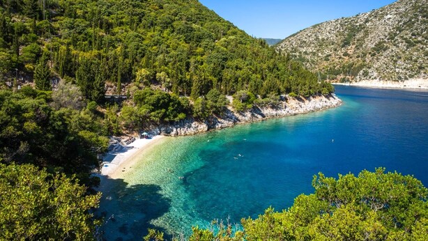 Un paysage côtier caractérisé par une mer turquoise aux eaux limpides, une plage de sable et des collines verdoyantes et densément boisées.