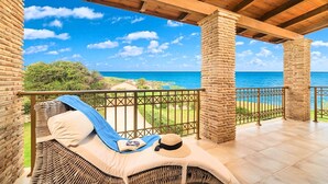 Un balcon avec un fauteuil en osier, une serviette bleue et un chapeau, offrant une vue sur la côte et un ciel dégagé.