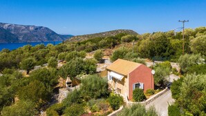 A coastal house with a red exterior, surrounded by dense greenery and a clear view of the sea. - Romantic Cottage with Private Pool and Garden near Vathy and Dexa Beach (Ithaca)