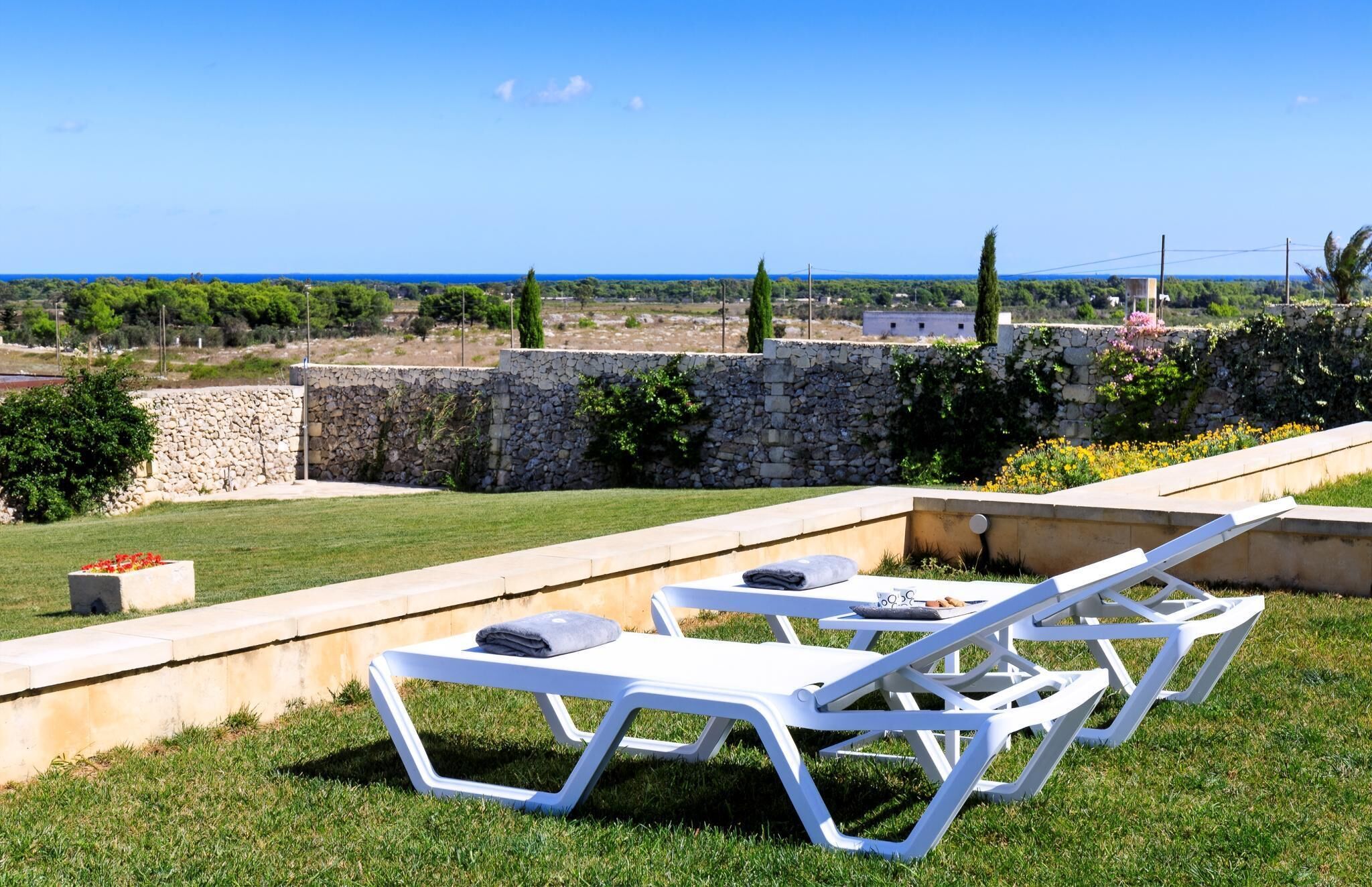 Um terraço com cadeiras de lounge brancas, uma parede de pedra e vista para o mar.