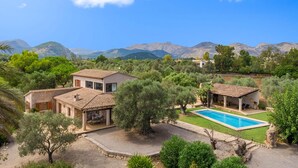 Eine Villa mit Swimmingpool, umgeben von üppiger Vegetation und Bergen im Hintergrund.