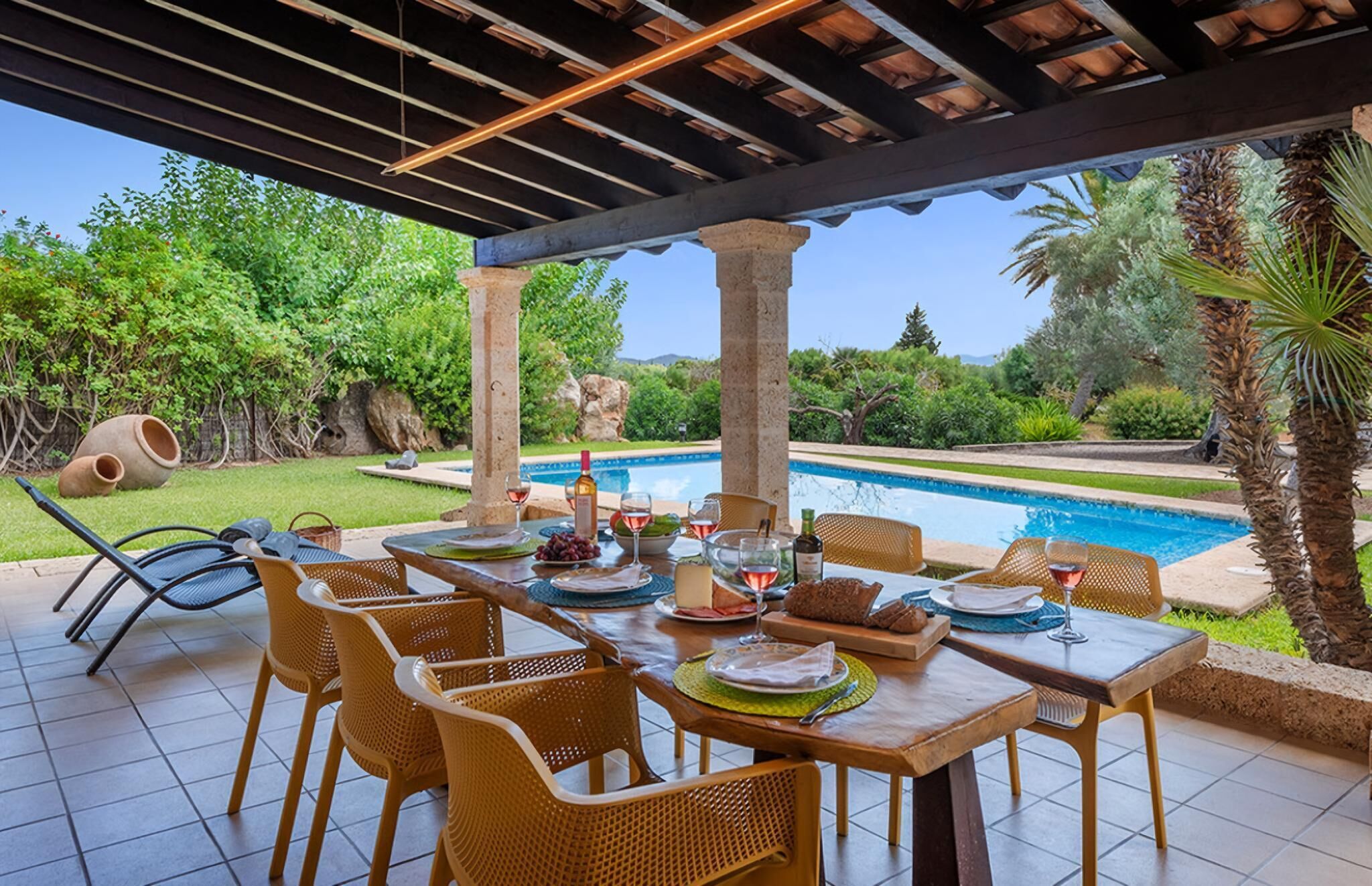 Un espace de restauration en plein air avec vue sur la piscine, comprenant une table dressée pour un repas, des chaises et une structure en forme de pergola.