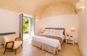 A bedroom with a bed, bedside tables, a chair, and a glass door leading to an outdoor area. - Stunning Valle d'Itria Retreat with Heated Pool, Outdoor Kitchen and Trullo Annexe (Brindisi)