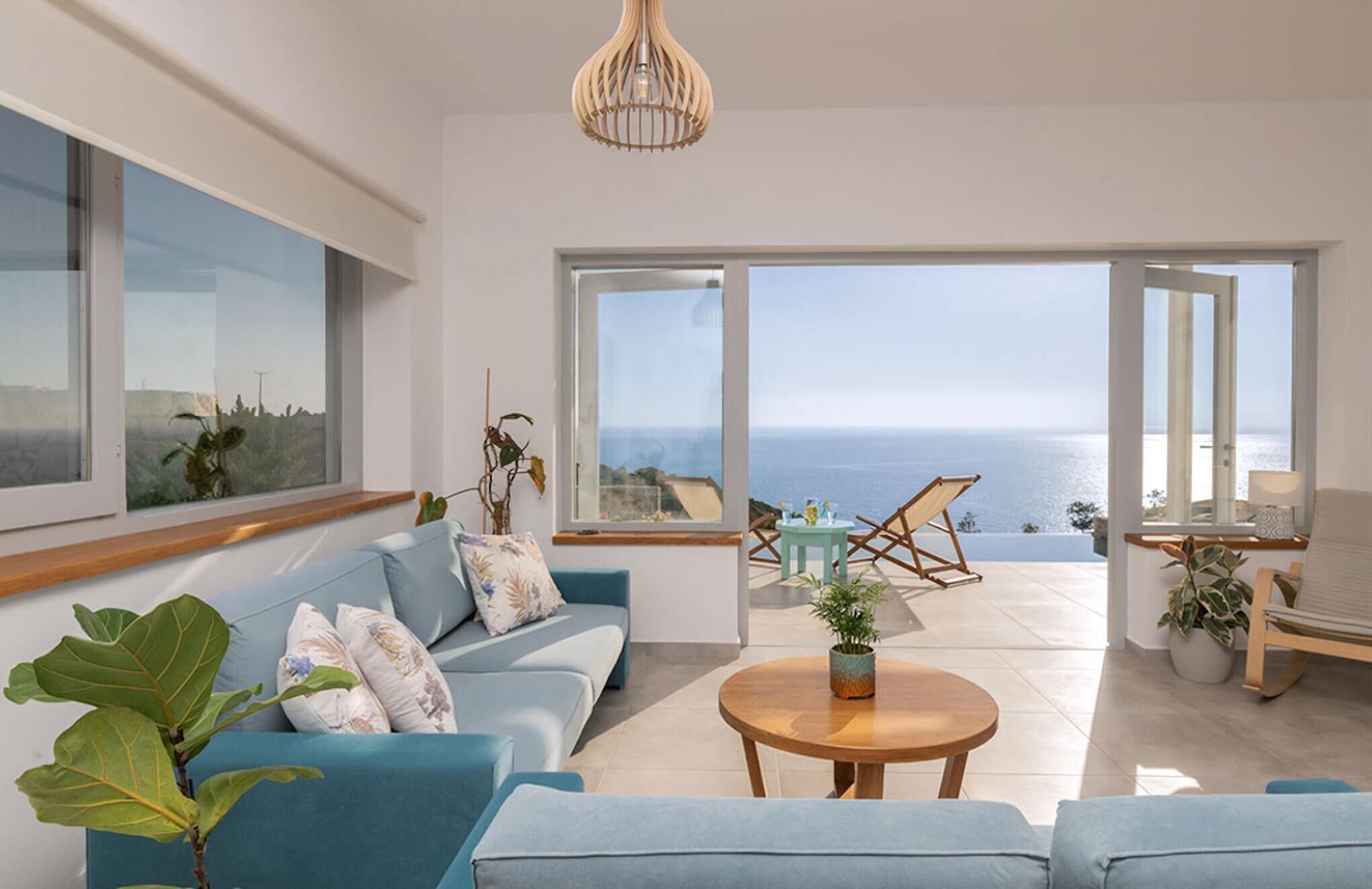 A modern living room with a sofa, a coffee table, and a view of the sea through large windows.