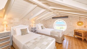 Ein Schlafzimmer mit zwei Betten, einer Holzkommode, einem Nachttisch, einer Lampe, einer Steinsäule und einem Fenster mit Blick.