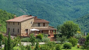 A stone house with a tiled roof, surrounded by lush greenery and hills in the background. - Villa Mille Desideri (Arezzo)