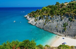 Een kustlandschap met helder turquoise water, rotskliffen en een zandstrand met parasols.