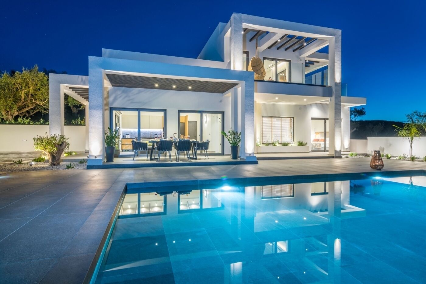 A modern two-story house with a swimming pool, outdoor seating, and large windows.