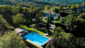 Ein Schwimmbecken, umgeben von einem gepflegten Garten, mit einem Steinhaus und Blick auf sanfte Hügel im Hintergrund.