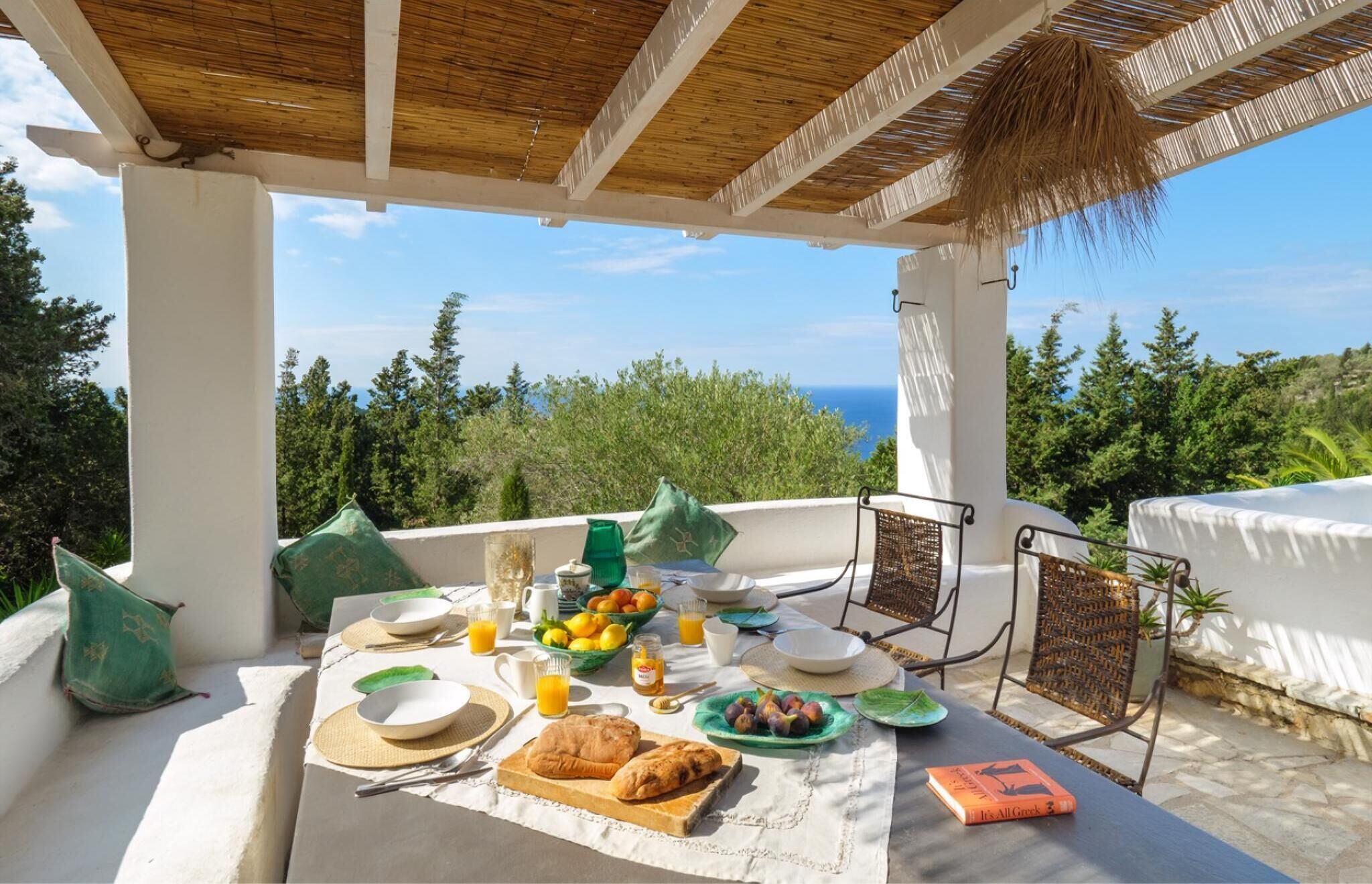Ein Frühstückstisch auf einer Terrasse mit Blick aufs Meer, einschließlich Tellern, Gläsern und einem Buch.