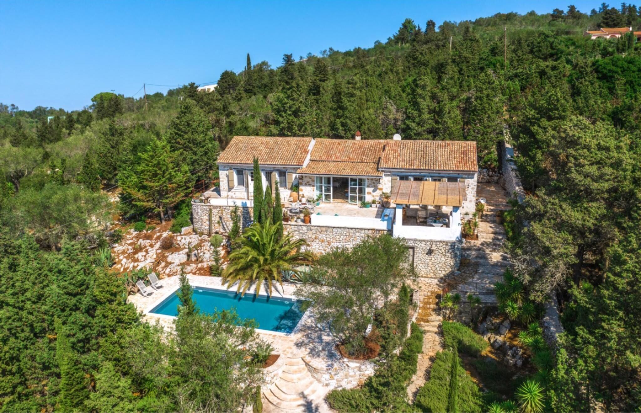 Una vila amb piscina envoltada d'arbres, situada en una zona elevada.