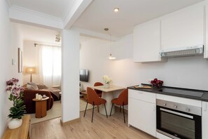 A modern kitchen with white cabinets, a built-in oven, and a dining area with a table and chairs. - This charming one-bedroom apartment is a bright and quiet retreat, facing a spacious courtyard. Fully furnished, it features a comfortable double bed. (MADRID)