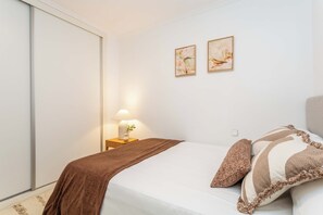 Ein Schlafzimmer mit einem Bett, einem Nachttisch mit Lampe und zwei gerahmten Bildern an der Wand.