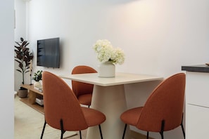 A dining area with a table, chairs, a vase with flowers, a television, and a plant. - This charming one-bedroom apartment is a bright and quiet retreat, facing a spacious courtyard. Fully furnished, it features a comfortable double bed. (MADRID)
