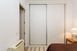 A bedroom with a bed, a bedside table with a lamp, a radiator, and a sliding door closet. - This charming one-bedroom apartment is a bright and quiet retreat, facing a spacious courtyard. Fully furnished, it features a comfortable double bed. (MADRID)