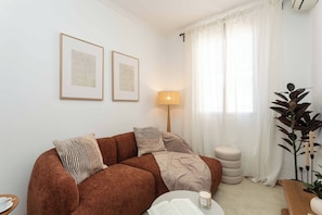 A cozy living room with a brown sofa, a side table with a cup, a lamp, and a large plant. - This charming one-bedroom apartment is a bright and quiet retreat, facing a spacious courtyard. Fully furnished, it features a comfortable double bed. (MADRID)