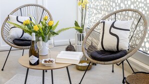 Zwei Korbstühle mit Kissen, ein Tisch mit einer Flasche, einem Buch und einer Schüssel mit Nüssen.