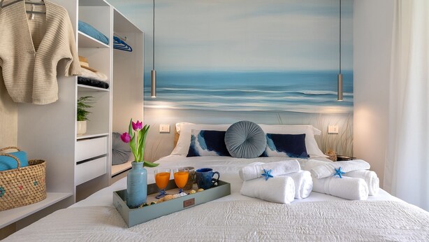 Ein Hotelzimmer mit Bett, Schrank, Tablett mit Frühstücksgegenständen und einem Meeresbild an der Wand.