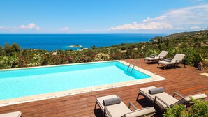Ein Swimmingpool mit Liegestühlen und Blick auf das Meer.