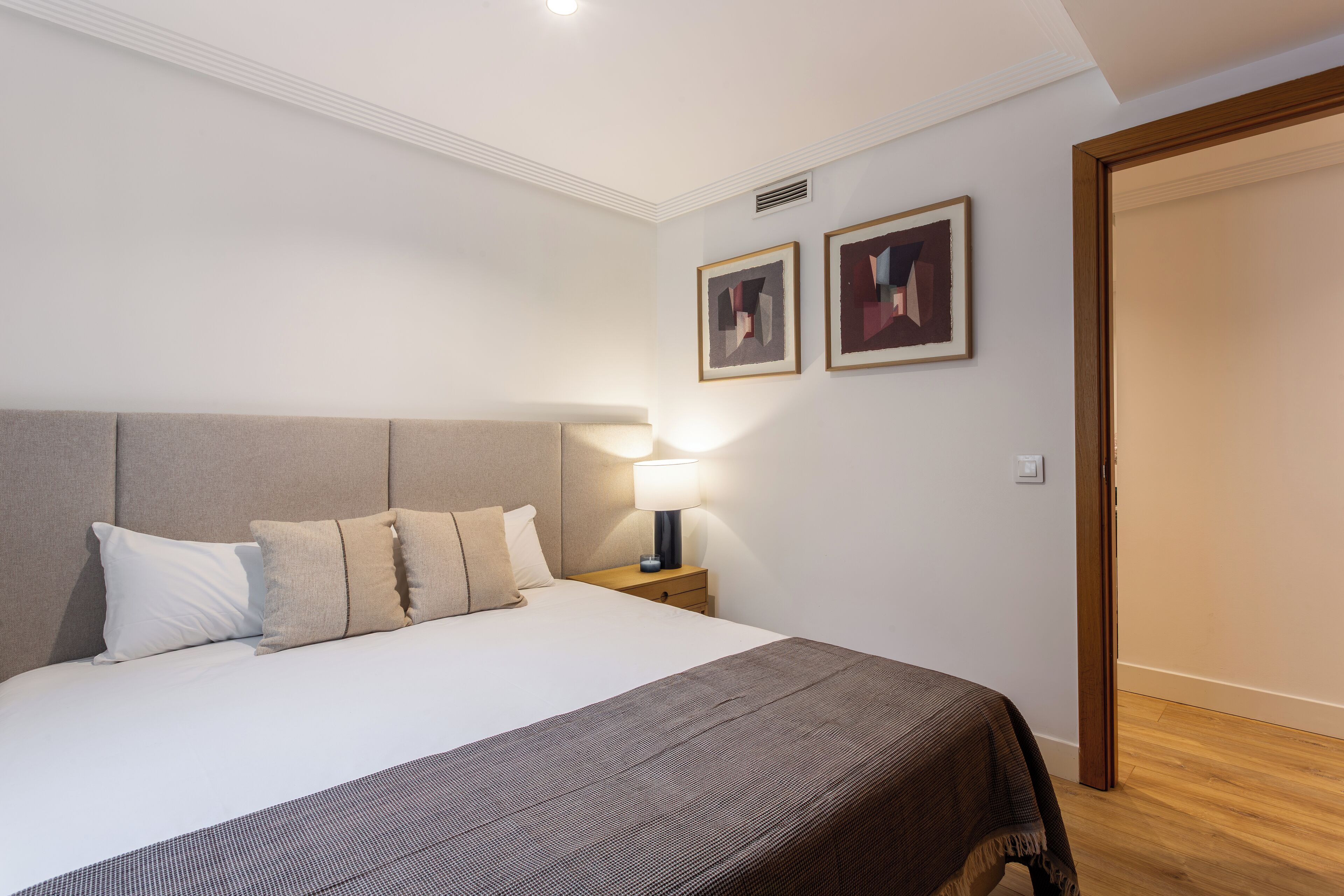 A neatly made bed with a headboard, a bedside lamp, and two framed pictures on the wall.