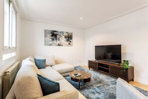 Ein modernes Wohnzimmer mit einem Ecksofa, einem Couchtisch, einem Flachbildfernseher und einem großen abstrakten Gemälde an der Wand.